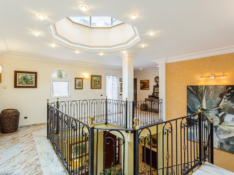 Palier avec sols en marbre, balustrade en fer forgé et verrière octogonale au plafond.