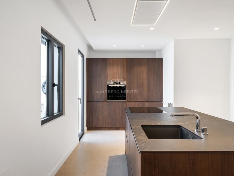 Cuisine moderne avec îlot en bois sombre, plan de travail noir, évier intégré et armoires encastrées.