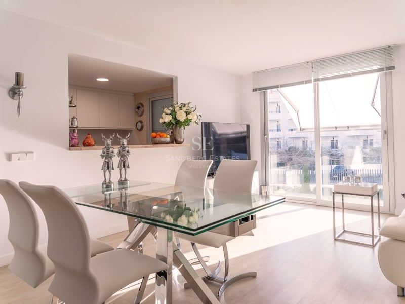 Espace salle à manger contemporain avec table en verre, chaises en cuir blanc et grandes baies vitrées.