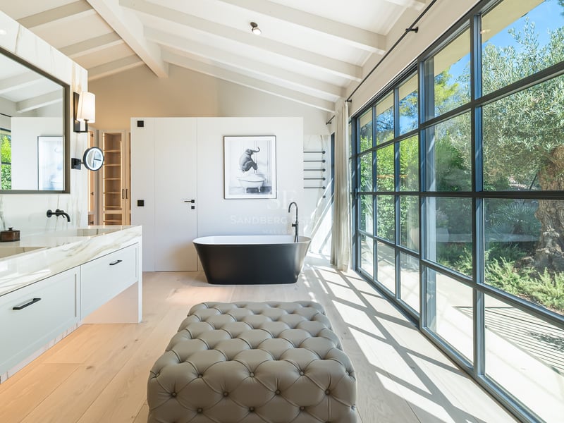 Salle de bains de luxe avec baignoire îlot noire, double vasque en marbre et grandes baies vitrées donnant sur un jardin.