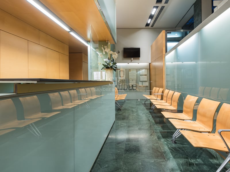 Modern reception area with frosted glass panels, light wood seating, and dark green marble flooring.