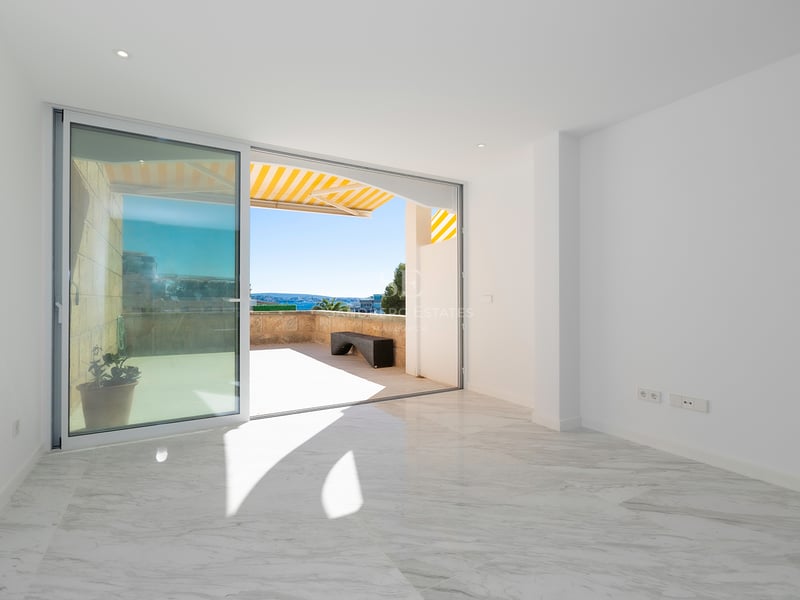 Pièce vide lumineuse avec sol en marbre blanc et grande baie vitrée coulissante ouvrant sur une terrasse ensoleillée.