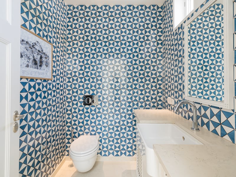 Petite salle de bain avec carreaux géométriques bleu et blanc, toilette moderne et vasque blanche.