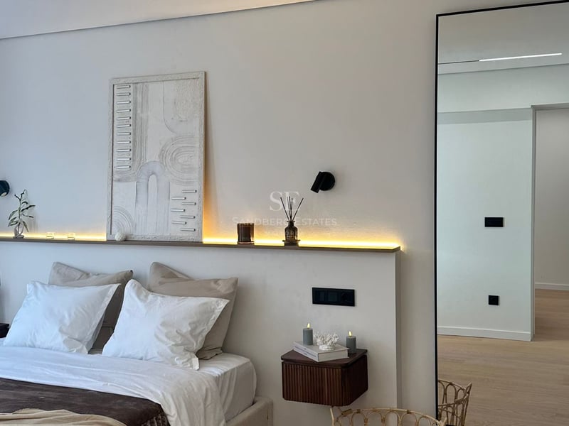 Chambre moderne avec lit blanc, rétroéclairage LED, œuvre d'art texturée et grand miroir sur parquet clair.