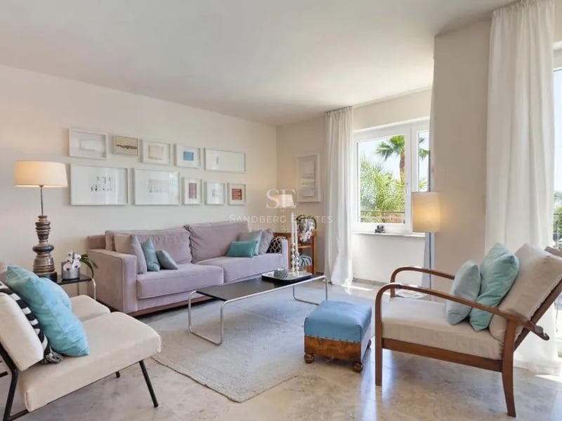 Salon spacieux avec sol en marbre, canapé mauve, touches de bleu et accès direct à une terrasse ensoleillée.