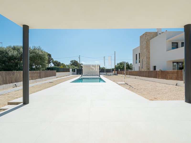 Vue depuis un porche couvert sur une piscine rectangulaire entourée de dalles blanches et de gravier dans une villa moderne.
