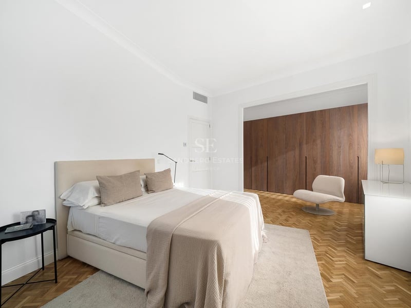 Chambre de maître minimaliste et lumineuse avec un grand lit, un sol en chevrons et des armoires en bois du sol au plafond.