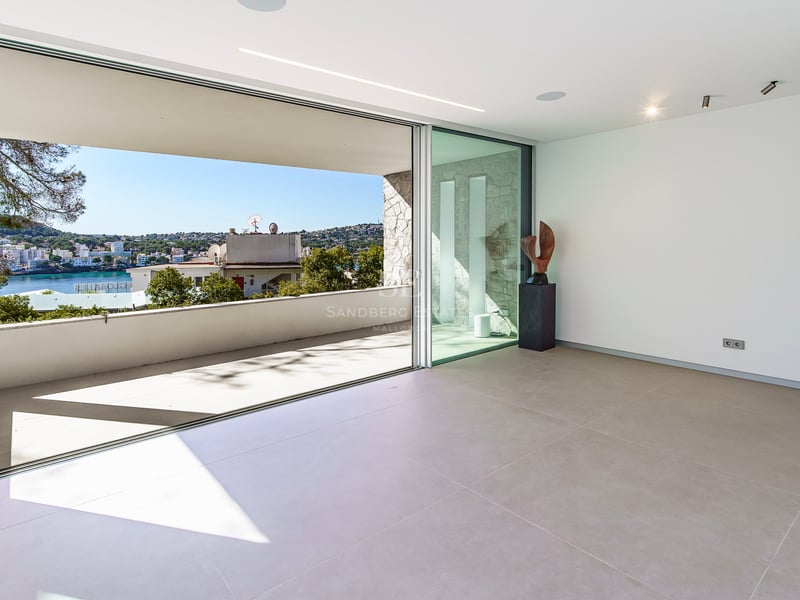 Intérieur minimaliste avec de grandes baies vitrées ouvrant sur une terrasse dominant la côte et la mer.