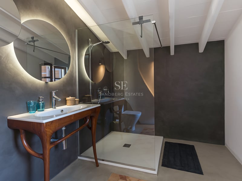 Modern bathroom featuring dark grey microcement walls, a circular backlit mirror, and a sculptural wooden vanity.