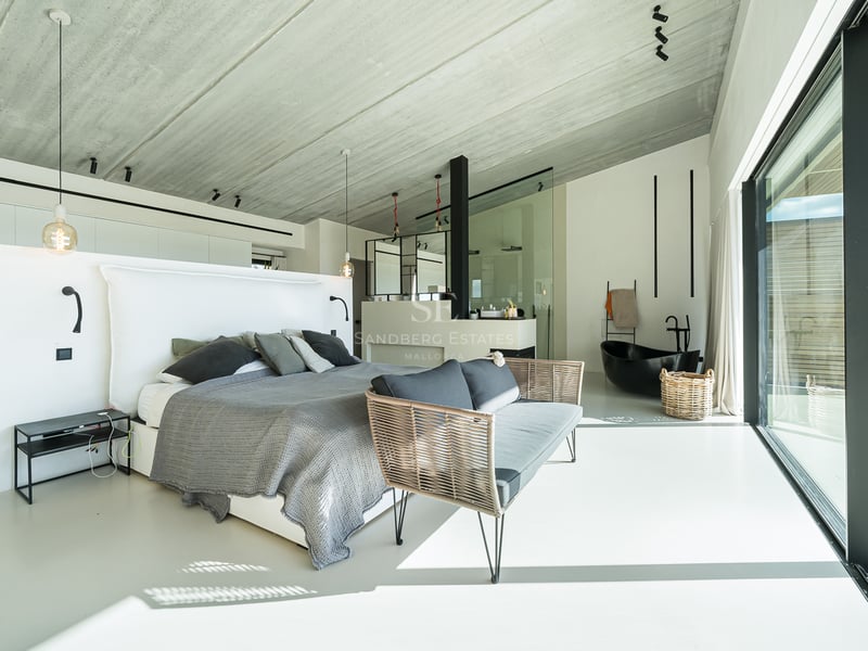 Chambre principale moderne avec lit gris, plafond en béton et baignoire îlot noire intégrée.