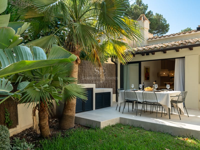 Table à manger extérieure sur une terrasse en pierre blanche entourée de palmiers et d'une façade de villa.