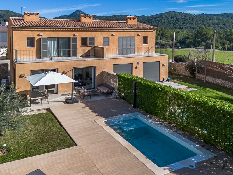 Vue aérienne d'une villa ocre avec piscine, terrasse en bois, jardin et montagnes en arrière-plan.