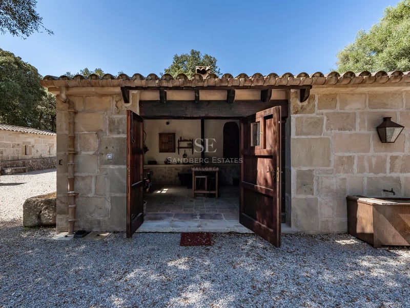 Petit bâtiment rustique en pierre avec portes en bois ouvertes et toit en tuiles sous un soleil radieux.