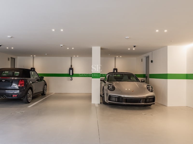 Vue intérieure d'un garage souterrain moderne avec une Porsche et une Mini, équipé de bornes de recharge murales.