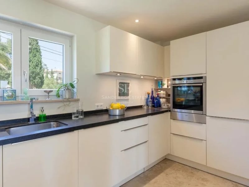 Cuisine contemporaine avec placards blancs sans poignées, plans de travail en granit noir et fenêtre sur le jardin.