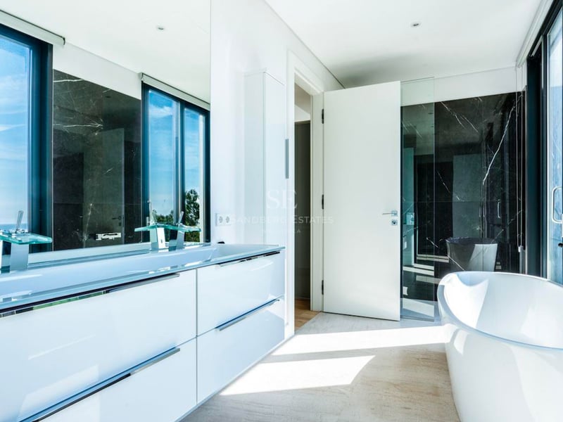 Salle de bain moderne avec baignoire îlot blanche, double vasque et mur en marbre noir avec vue sur la mer.