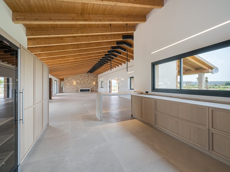 Intérieur spacieux avec sol en pierre claire, haut plafond voûté à poutres en bois, mur de cheminée en pierre et menuiserie.