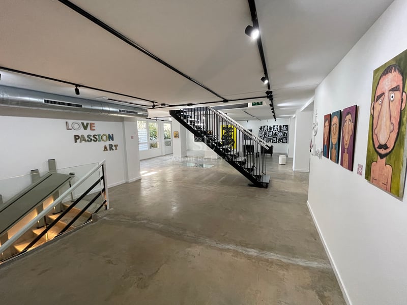 Espace industriel avec sols en béton poli, escalier en métal noir, murs blancs décorés d'art et éclairage sur rails.