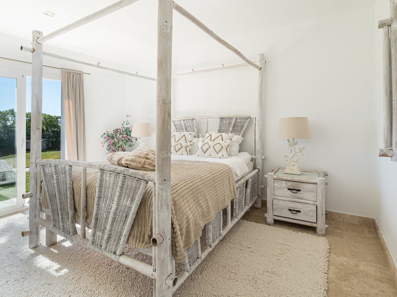 Chambre lumineuse avec lit à baldaquin en bambou blanc, textures tissées et accès direct au jardin.