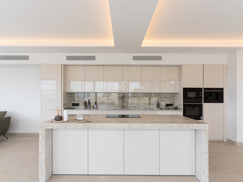 Cuisine minimaliste blanche avec îlot central en marbre et éclairage de plafond indirect dans une villa de luxe.
