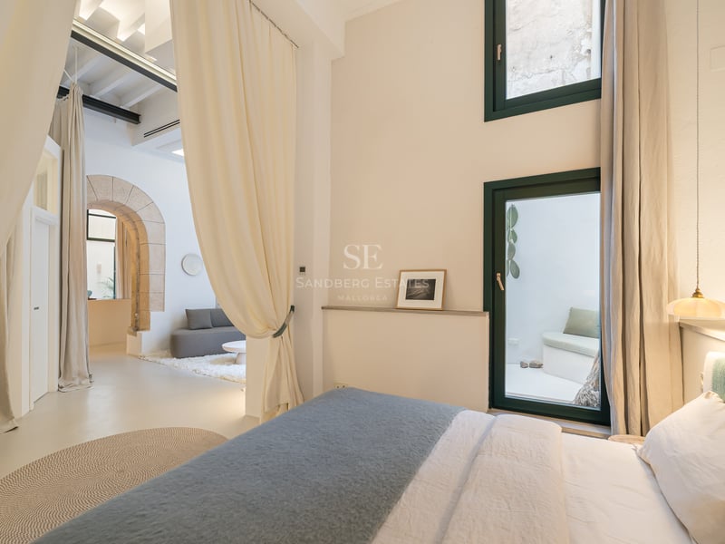 Chambre contemporaine avec une arche en pierre, de hauts plafonds, de grands rideaux crème et une décoration minimaliste.
