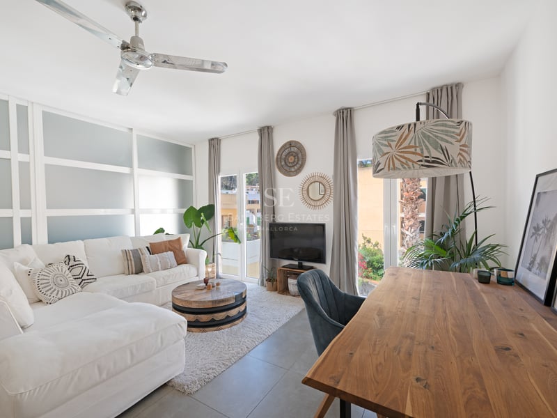 Salon moderne avec canapé blanc, bureau en bois naturel et cloison en verre dépoli ouvrant sur un balcon.