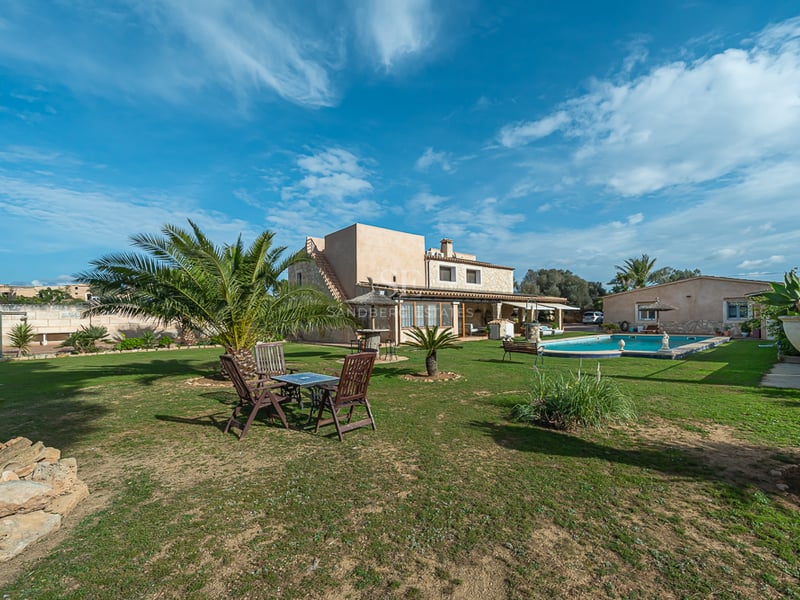 Exteriör av en rustik villa med stor gräsmatta, palmer, privat pool och utemöbler.