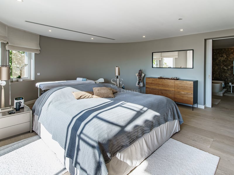 Chambre de maître contemporaine avec linge gris, buffet en bois et vue sur la salle de bain attenante en pierre naturelle.