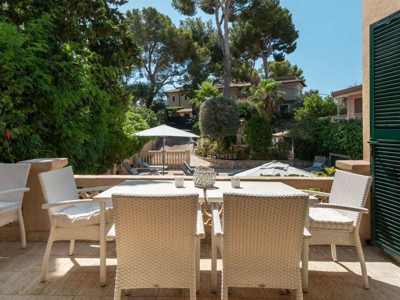 Salon de jardin en osier blanc sur une terrasse dallée de pierre surplombant un jardin méditerranéen et la piscine.