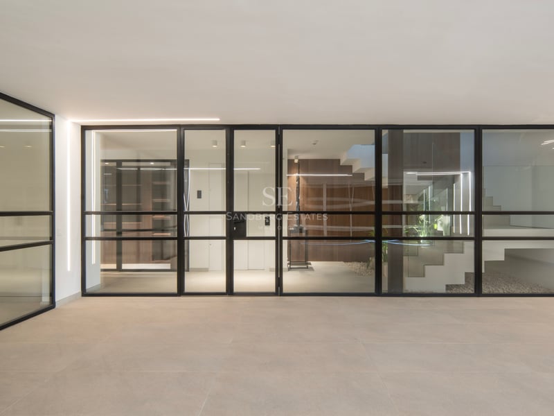 Entrée moderne avec parois vitrées à cadres noirs, carrelage beige et bandes lumineuses LED verticales.