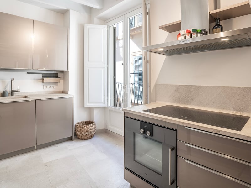 Cuisine moderne lumineuse avec placards taupe brillants, plans de travail en pierre et porte-fenêtre sur balcon.