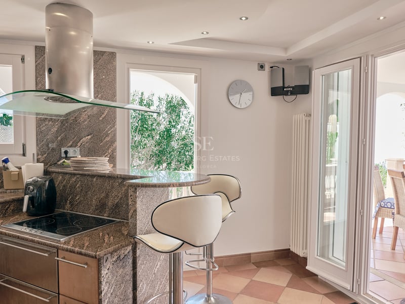 Cuisine moderne avec plans de travail en granit, bar et porte s'ouvrant sur une terrasse ombragée.