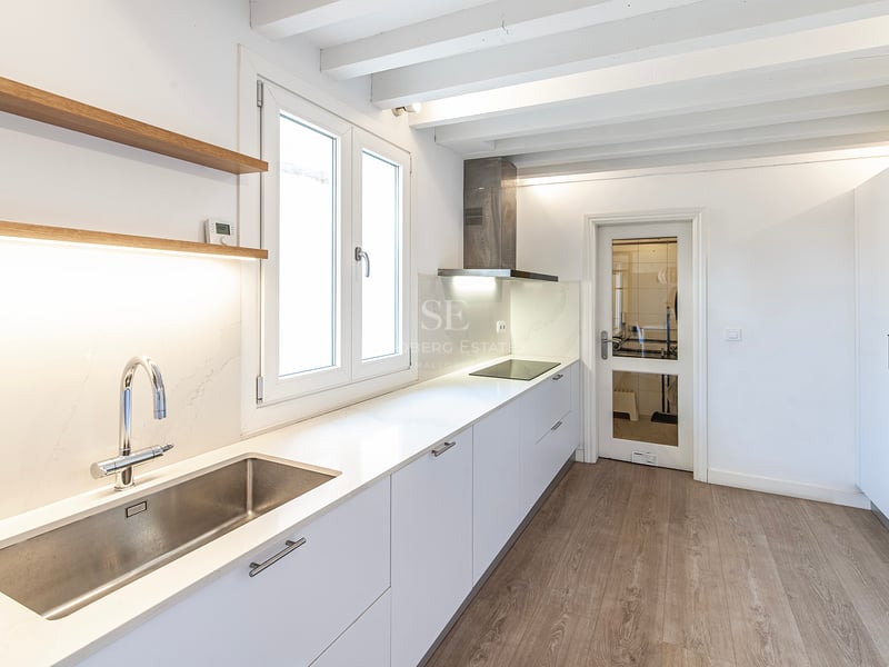 Cuisine moderne lumineuse avec placards blancs, plans de travail en quartz et poutres de plafond peintes en blanc.