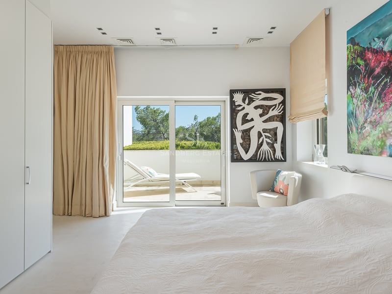 Chambre moderne et lumineuse avec murs blancs, baies vitrées coulissantes ouvrant sur une terrasse et art coloré.