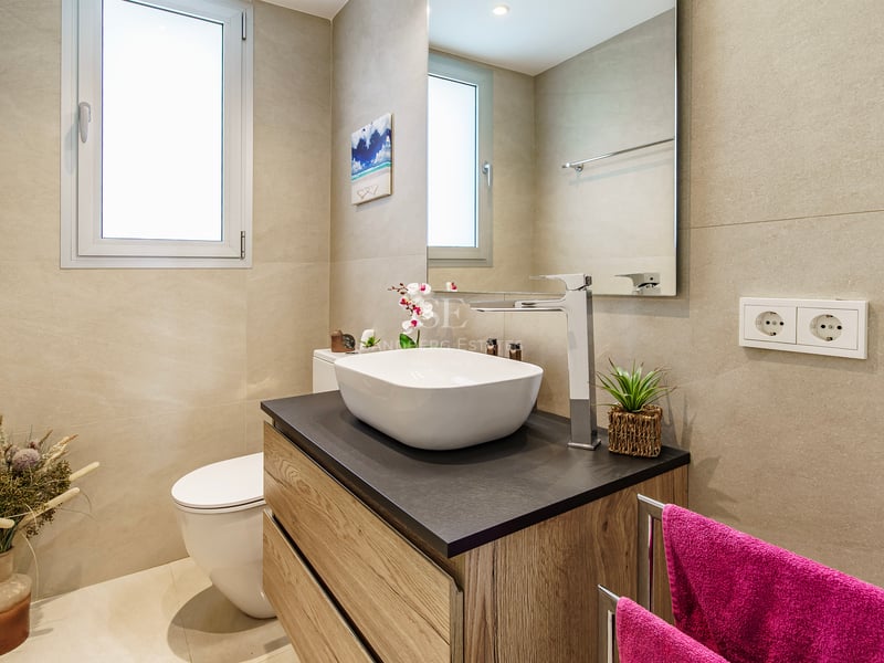 Salle de bain moderne équipée d'une vasque blanche, d'un meuble en bois, d'un grand miroir et de murs beiges.