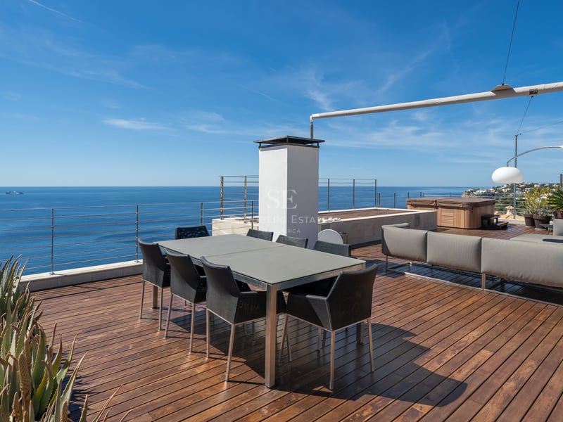 Terrasse moderne avec parquet en bois, table à manger, coin salon et garde-corps en verre surplombant la mer.