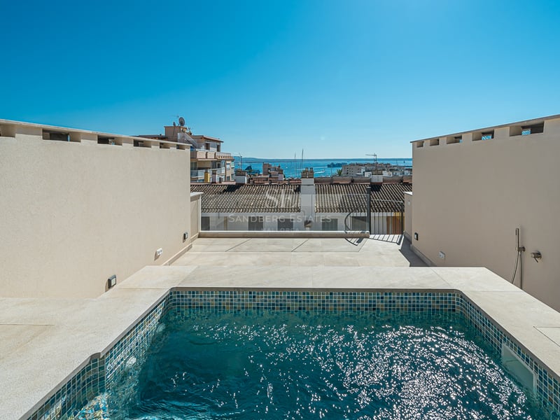 Terrasse moderne sur le toit avec piscine en mosaïque bleue et vue sur les toits de la ville et la mer.