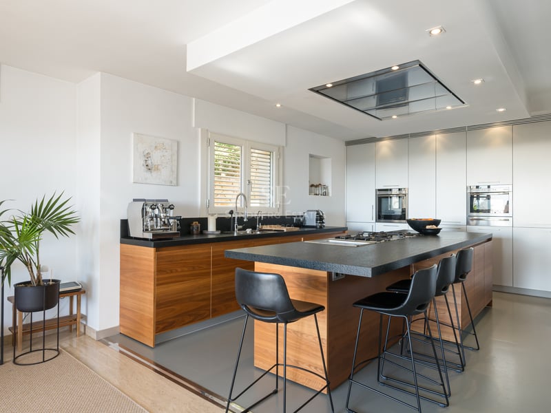 Cuisine moderne avec menuiserie en bois, îlot en granit noir avec tabourets et appareils intégrés.