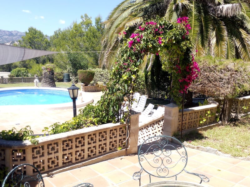 Piscine ovale entourée d'une terrasse en terre cuite, arche de bougainvilliers et vue sur les montagnes.