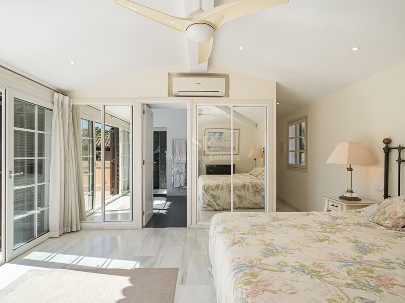 Chambre lumineuse avec sol en marbre blanc, armoires à miroirs et portes coulissantes ouvrant sur une terrasse.