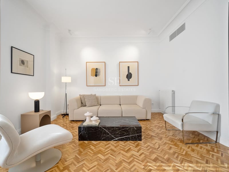 Salon lumineux avec murs blancs, parquet à bâtons rompus, canapé beige et une table basse en marbre noir remarquable.