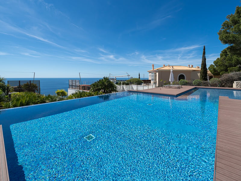 Grande piscine à débordement en mosaïque bleue donnant sur l'horizon marin avec terrasse en pierre.