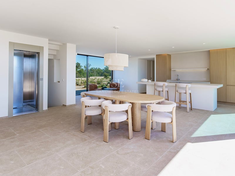 Salle à manger lumineuse avec table ovale en bois, chaises blanches et baies vitrées donnant sur le jardin.