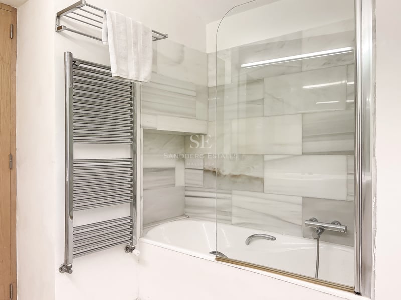Baignoire blanche avec paroi en verre, carrelage mural en marbre gris et blanc et sèche-serviettes chromé.