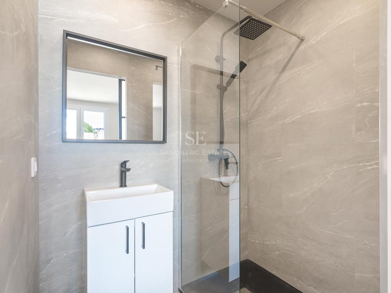 Salle de bains moderne avec carrelage gris effet pierre, paroi de douche en verre et robinetterie noire mate.