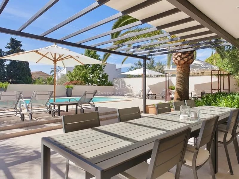 Pergola moderne grise abritant une table à manger extérieure à côté d'une piscine avec chaises longues et palmiers.