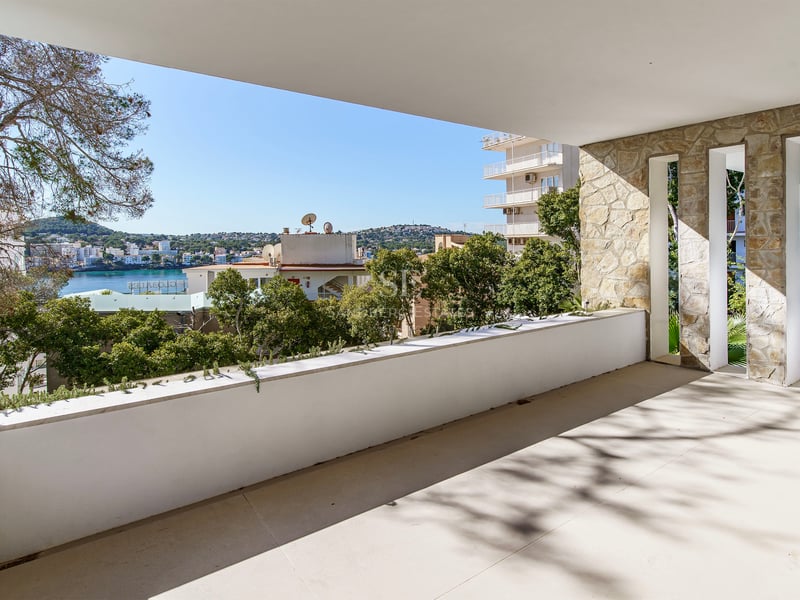 Terrasse couverte avec mur en pierre naturelle et garde-corps blanc donnant sur une baie bleue et une ville côtière.