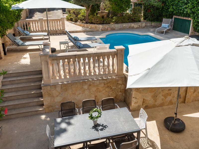 Terrasse ensoleillée sur plusieurs niveaux avec piscine, chaises longues et coin repas extérieur aux murs de pierre.