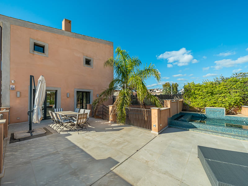 Terrasse méditerranéenne avec sol en pierre, salle à manger extérieure, palmier et petite piscine carrelée sous un ciel bleu.