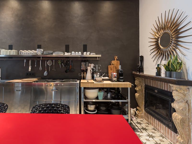 Modern kitchen featuring stainless steel cabinets, a dark textured wall, a red table, and an ornate stone fireplace.